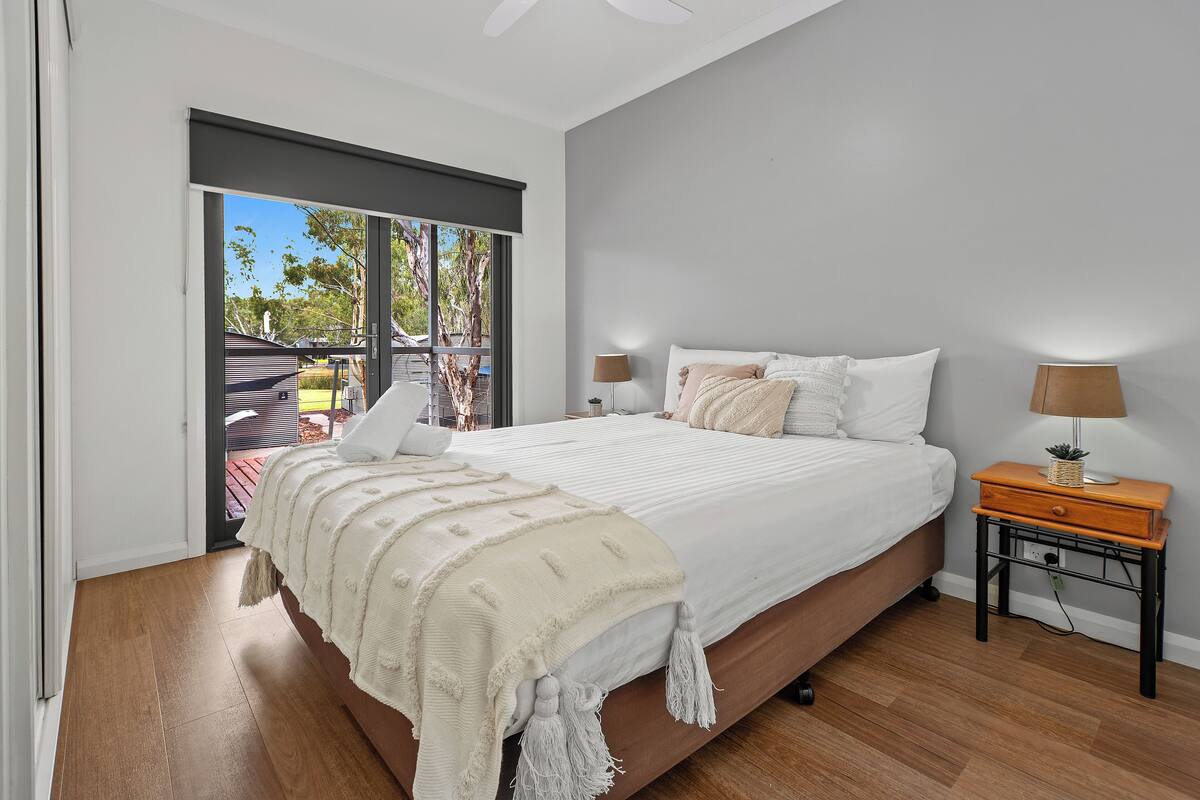 A bedroom with a large bed, two bedside tables, a ceiling fan, and a sliding glass door leading to an outdoor area.