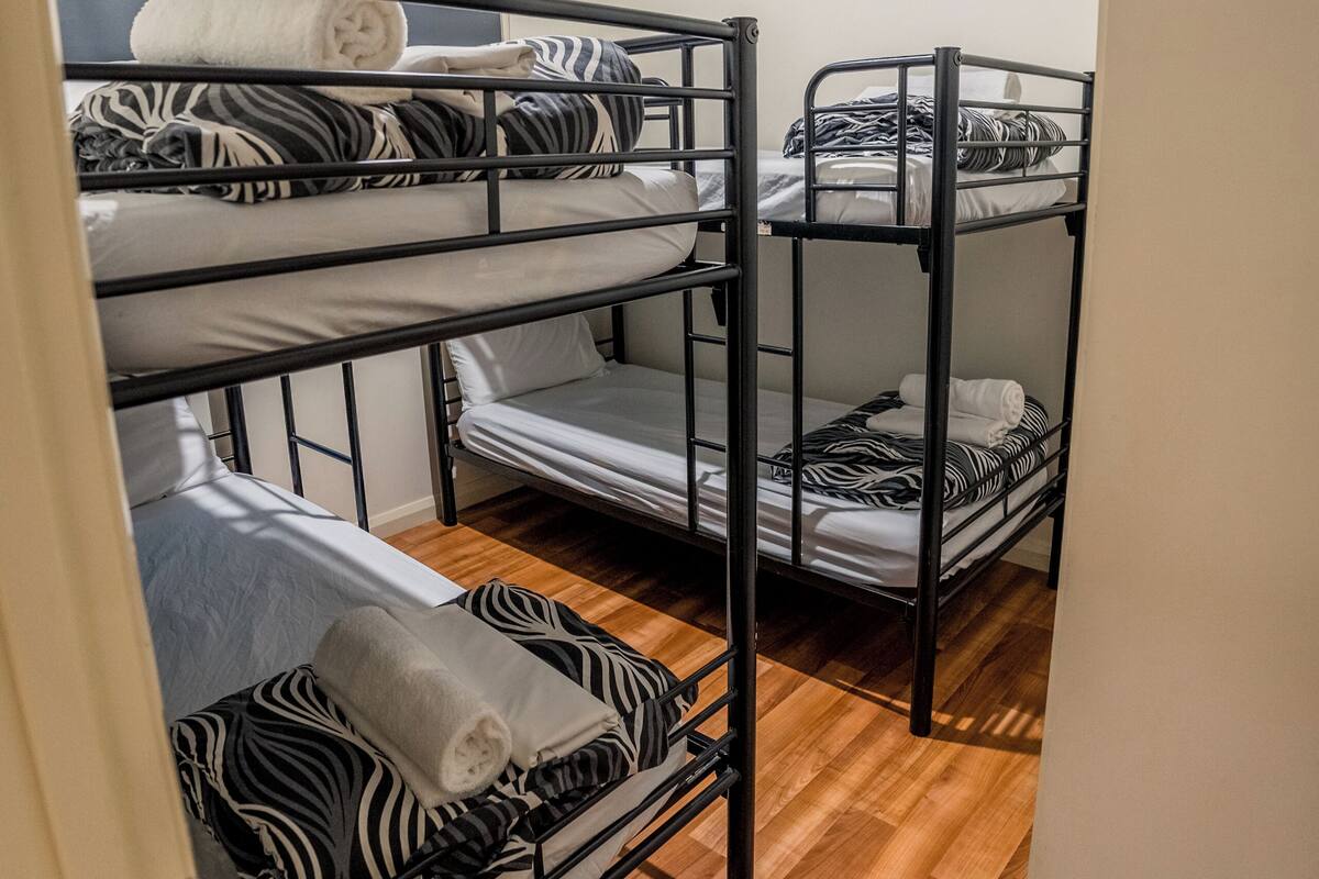 A bunk bed room with a wooden floor, white walls, and a door partially visible.