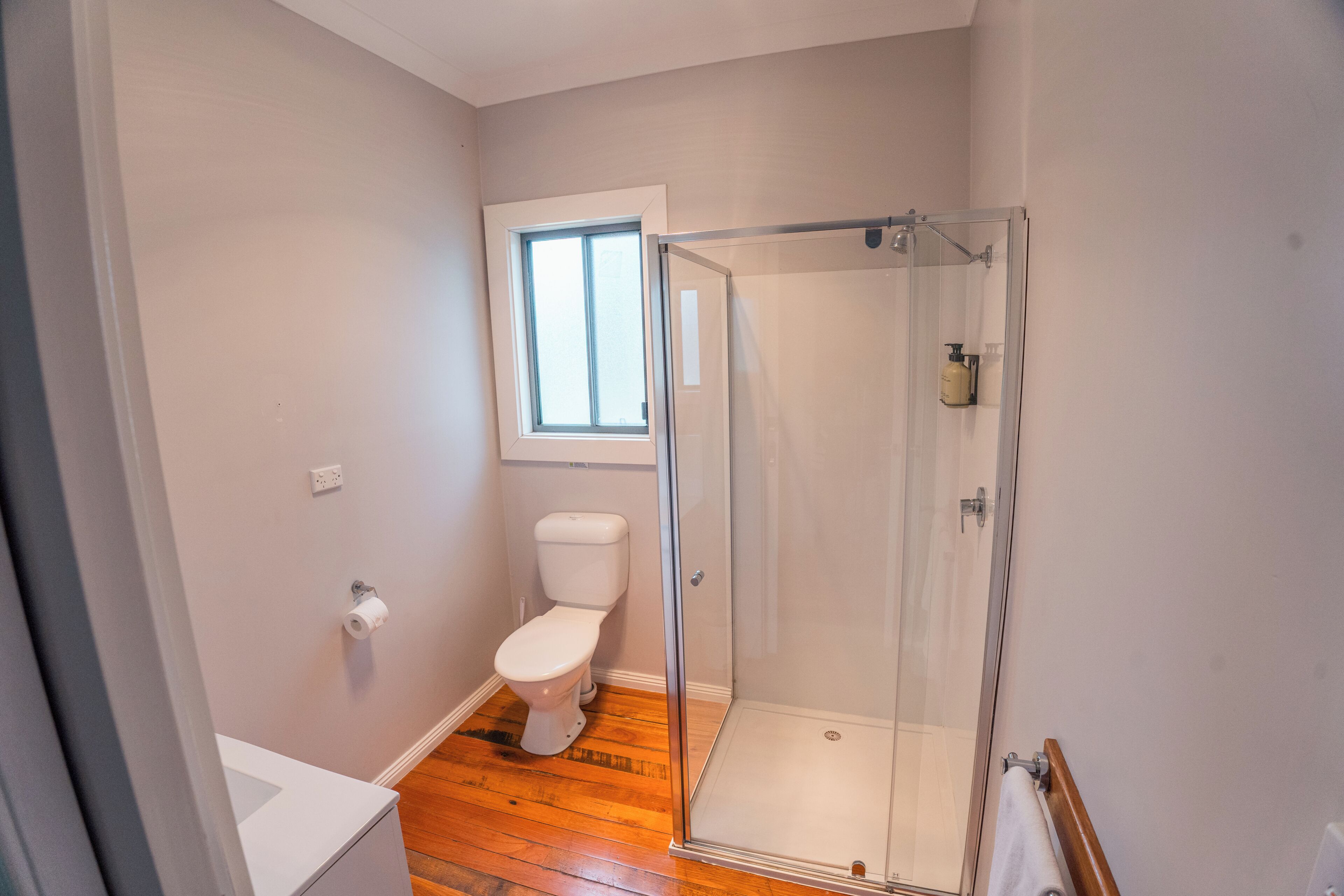 A bathroom with a toilet, a shower with a glass door, and a window.