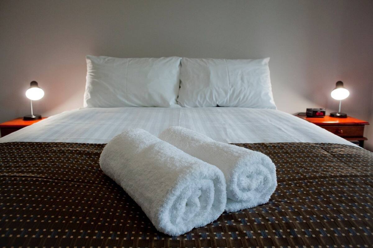 A neatly made bed with white linens, two rolled towels, and two bedside lamps on wooden nightstands.