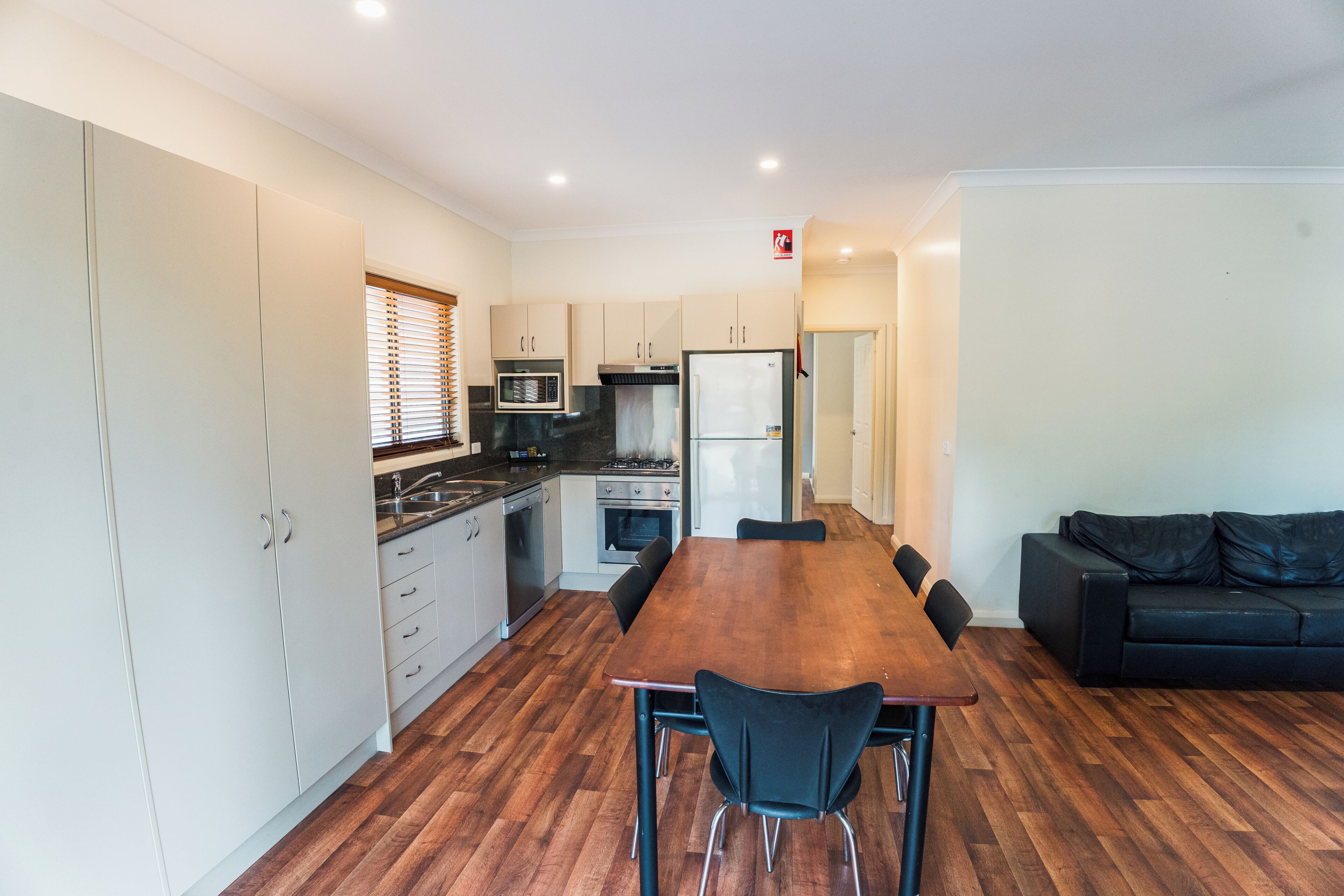 A modern kitchen with white cabinets, a dining table, and a black sofa.