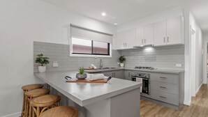 A modern kitchen with white cabinetry, a central island with stools, a window above the sink, and a built-in oven.