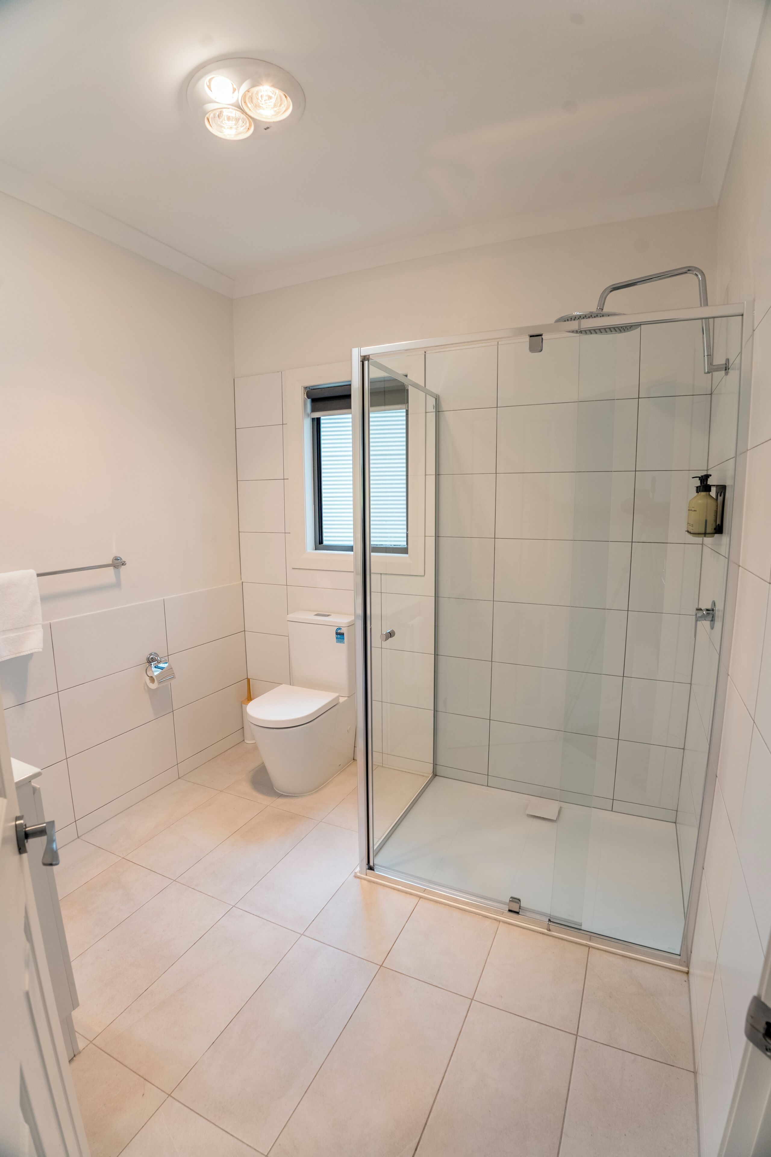 A modern bathroom with a glass shower enclosure, a toilet, and a window.