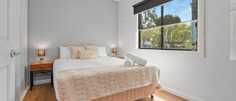 Un dormitorio con cama, mesita de noche, ventana y puerta.