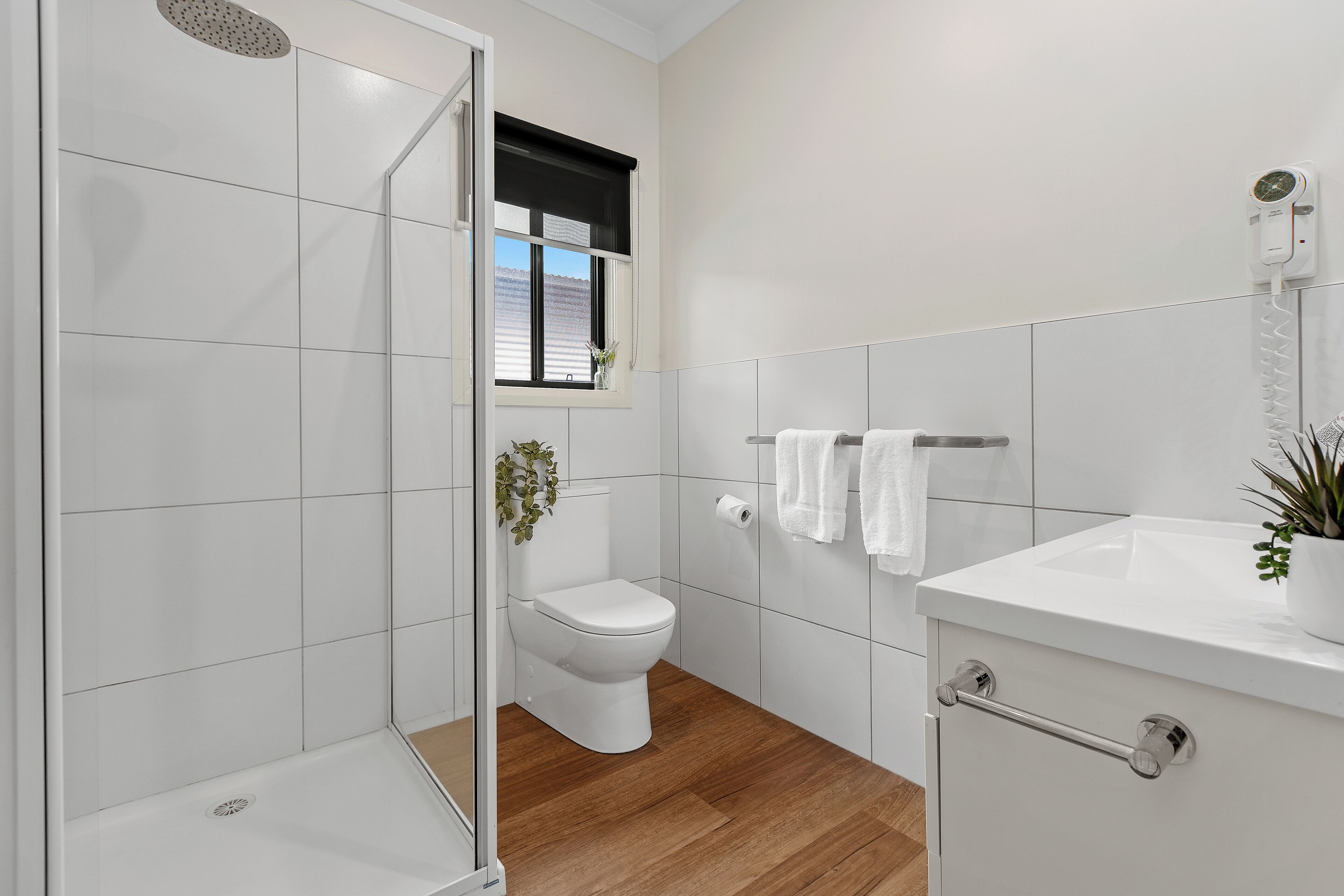 Un baño moderno con cabina de ducha de vidrio, inodoro, lavamanos y ventana con vistas.