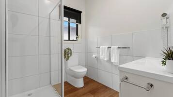 A modern bathroom with a glass shower enclosure, a toilet, a sink, and a window with a view.