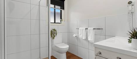 Un baño moderno con cabina de ducha de vidrio, inodoro, lavamanos y ventana con vistas.