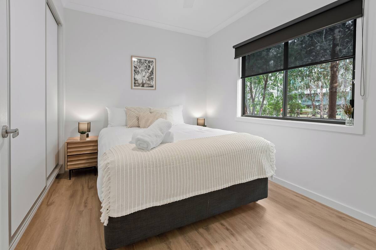 A bedroom with a bed, bedside tables, a window with a view, and a door.