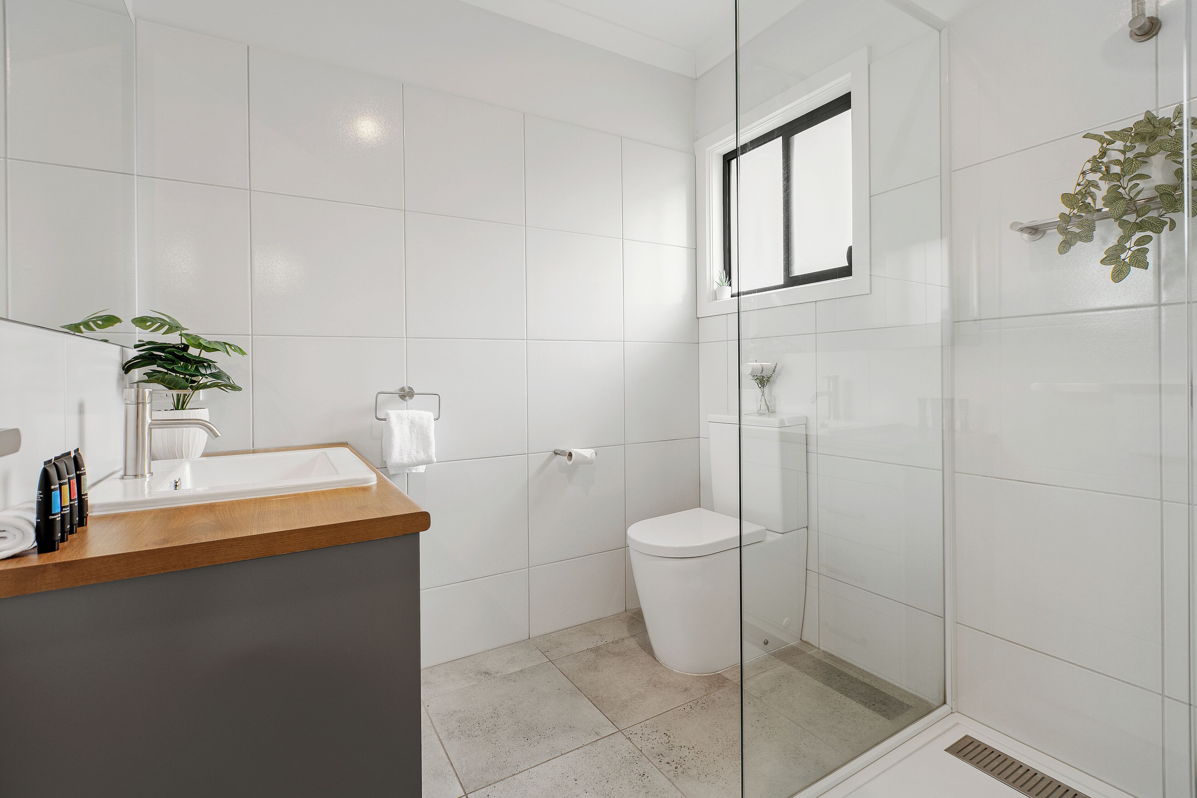 A modern bathroom with a glass shower enclosure, a white toilet, and a wooden countertop with toiletries.
