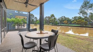 A covered outdoor seating area with a table and chairs, overlooking a body of water and trees.