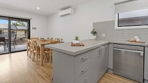 A modern kitchen with a built-in dishwasher, a dining area with wooden chairs, and a large window.