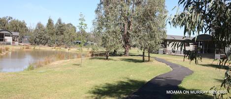 A pathway leading to a building with a pond and trees in the background.