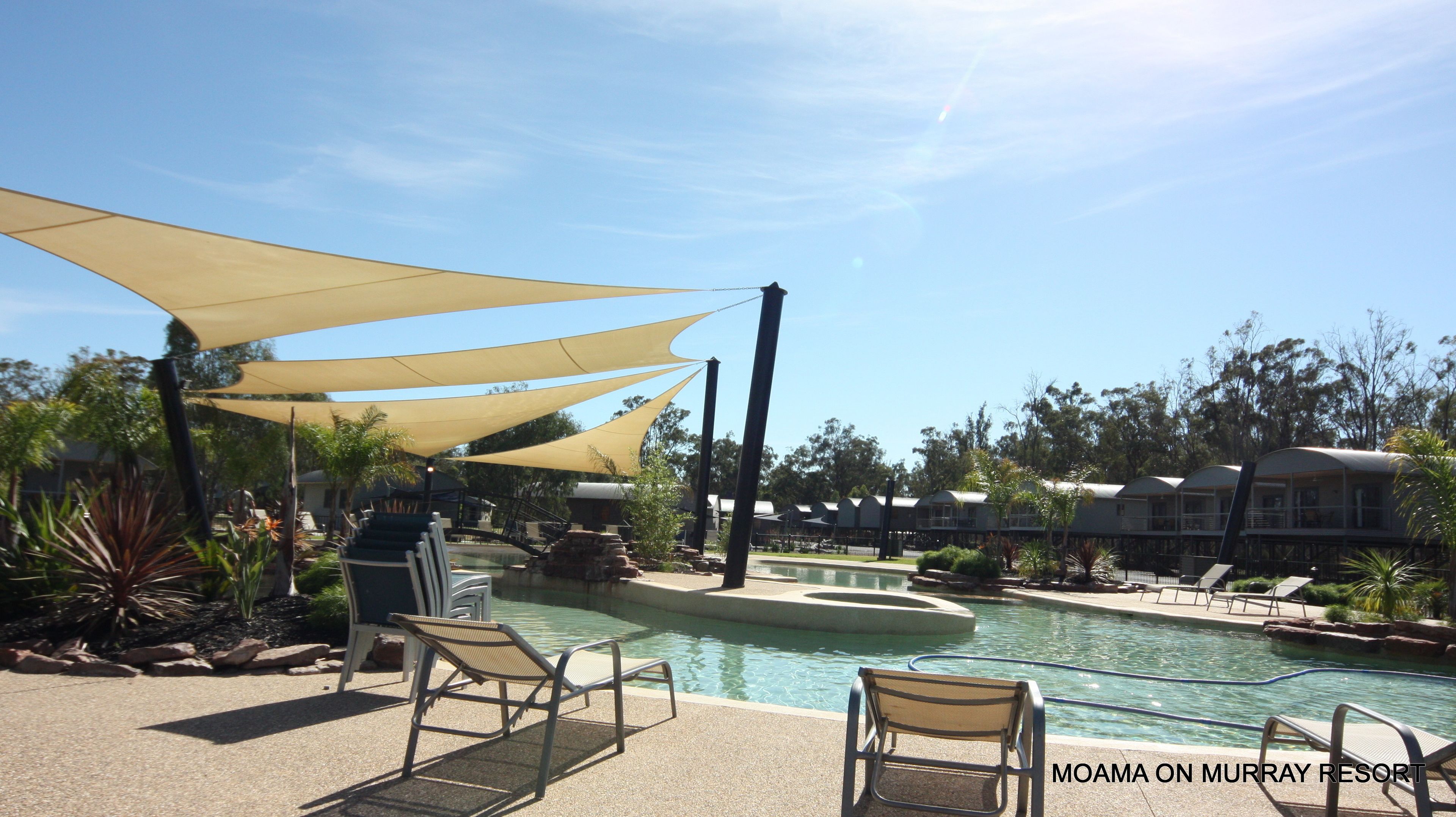 Un espace piscine au Moama on Murray Resort, avec des chaises longues, des zones ombragées et un ciel dégagé.