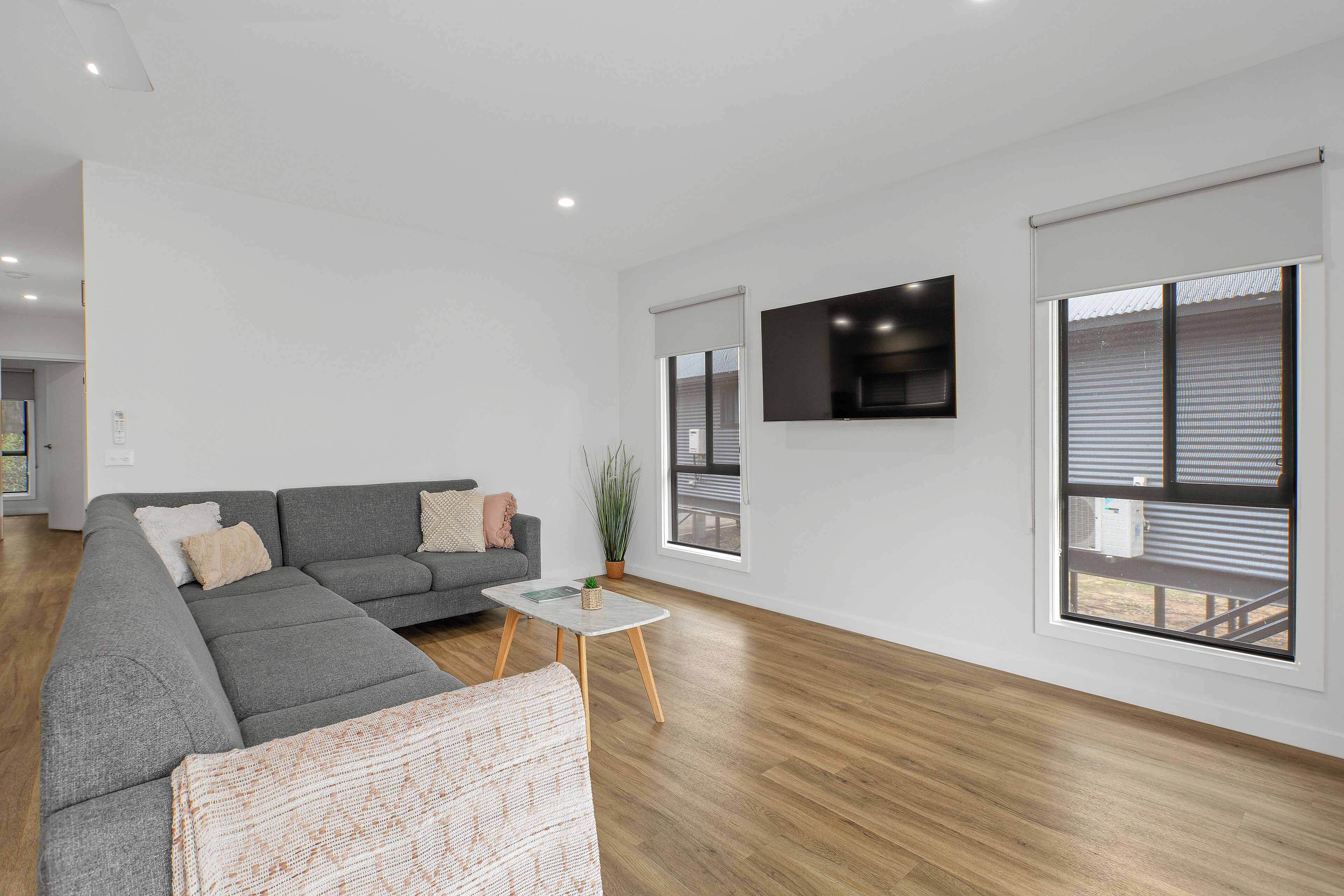 A modern living room with a grey sectional sofa, a small coffee table, and a flat-screen TV mounted on the wall.