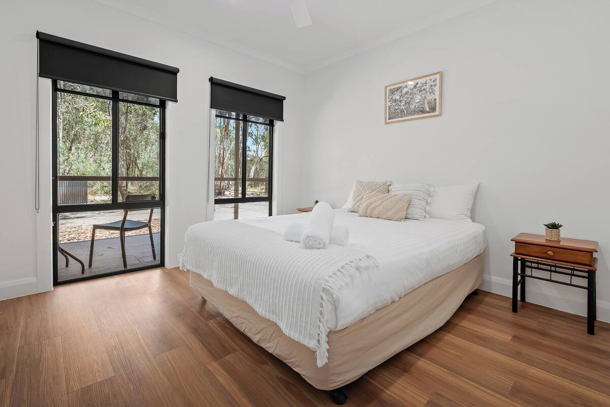 A bedroom with a large bed, a small bedside table, and a view through a sliding door to an outdoor patio.