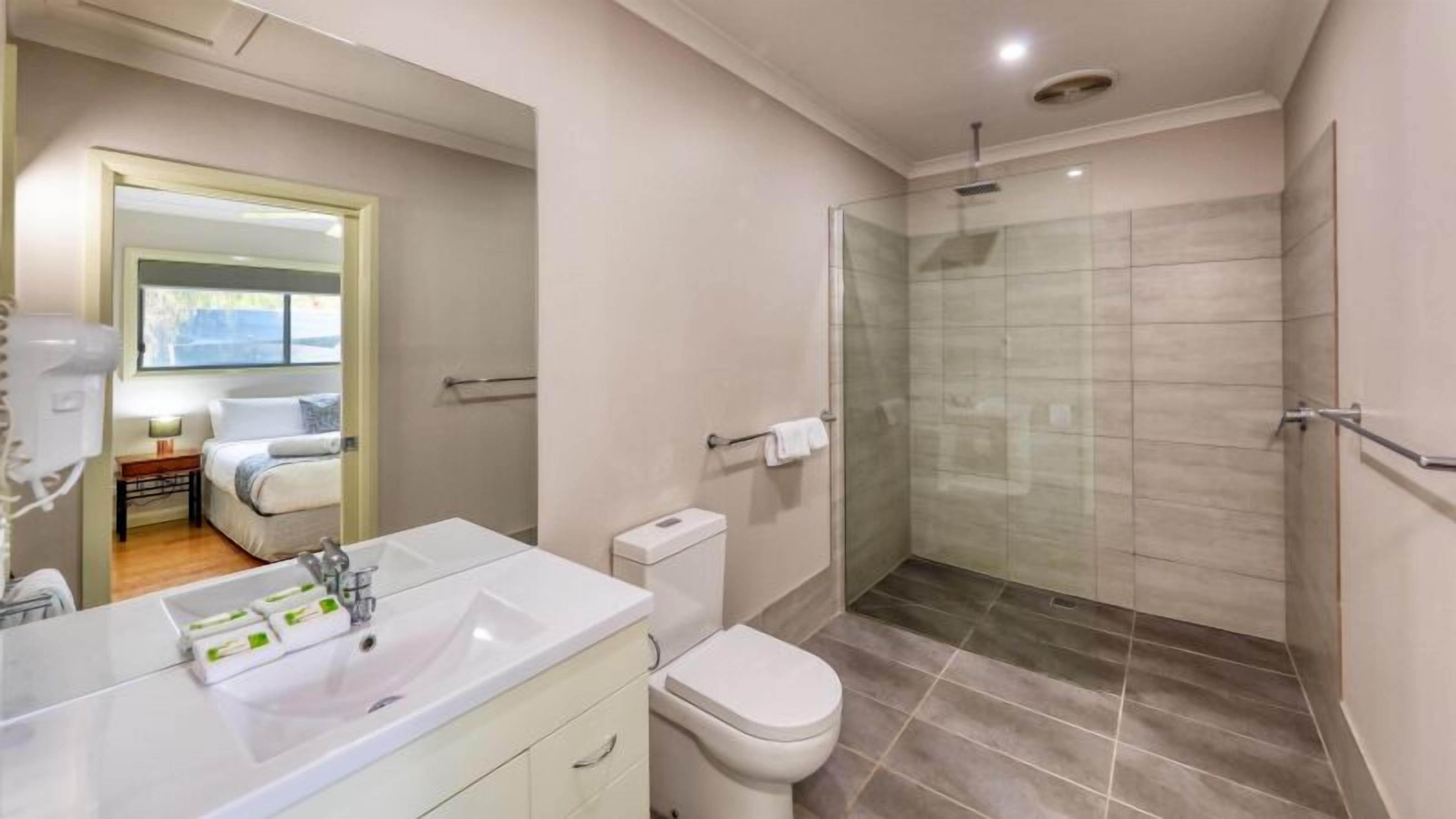 A modern bathroom with a glass-enclosed shower, a white sink with a mirror, and a toilet.