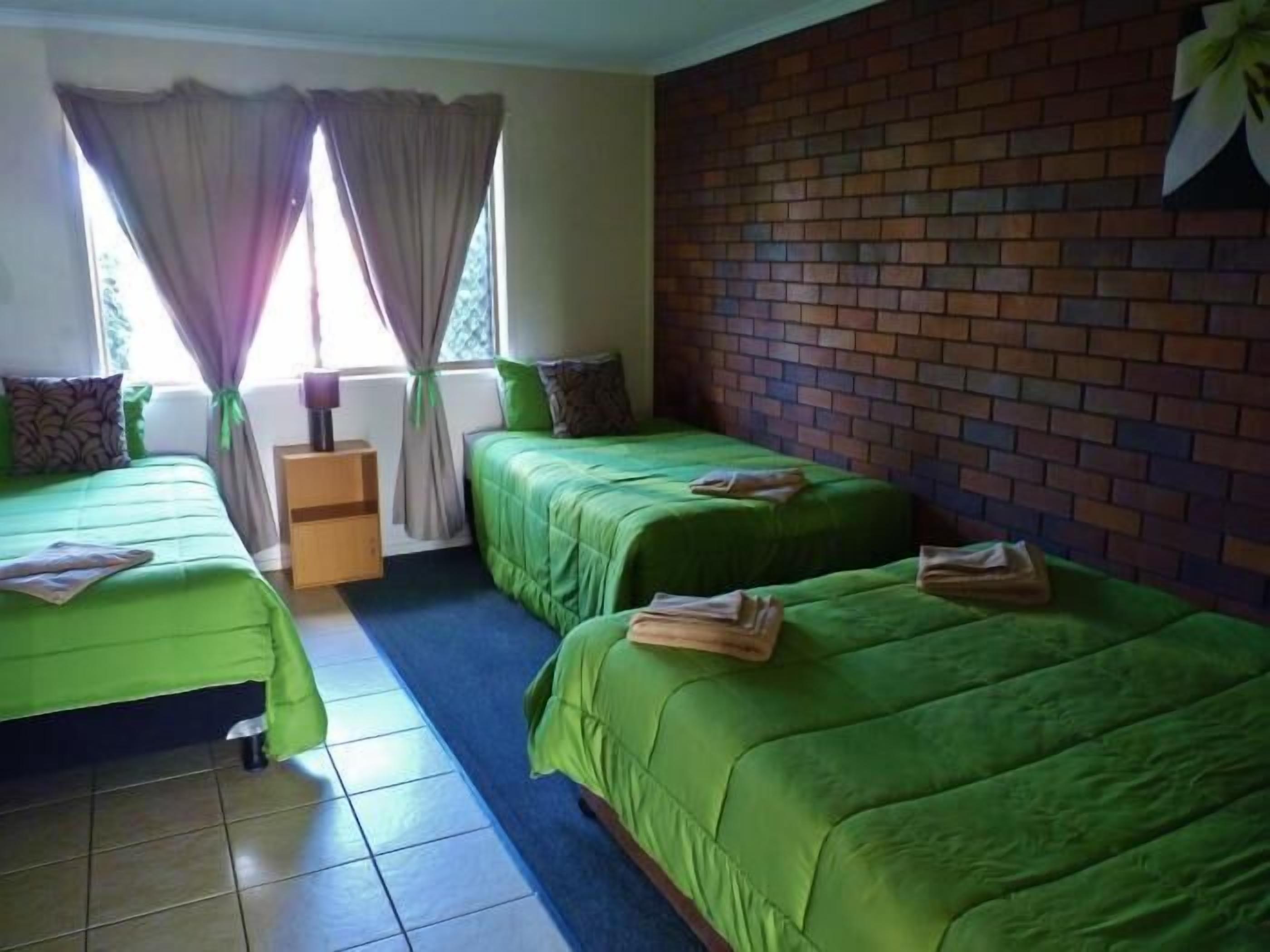 Una habitación con dos camas verdes, una mesita de noche de madera y una pared de ladrillo.