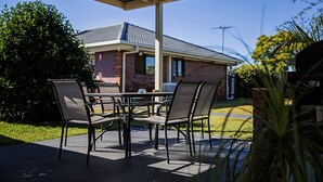 Un patio al aire libre con una mesa y sillas, una zona cubierta y un edificio de ladrillo al fondo.