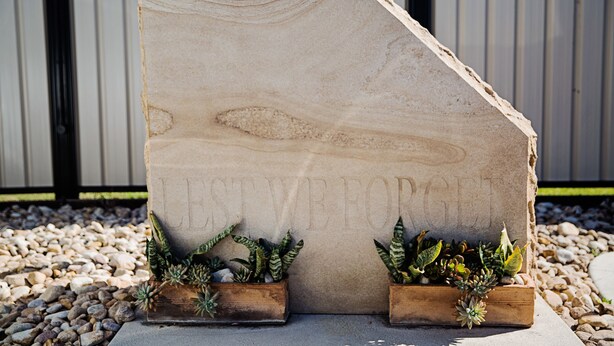 A stone structure with the inscription "LEST WE FORGET" and two wooden planters with succulents.