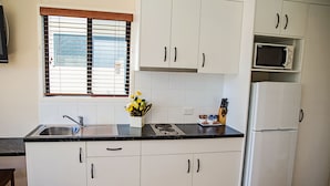 Una cocina con gabinetes blancos, encimera negra, un lavamanos, una estufa, un microondas y un refrigerador.