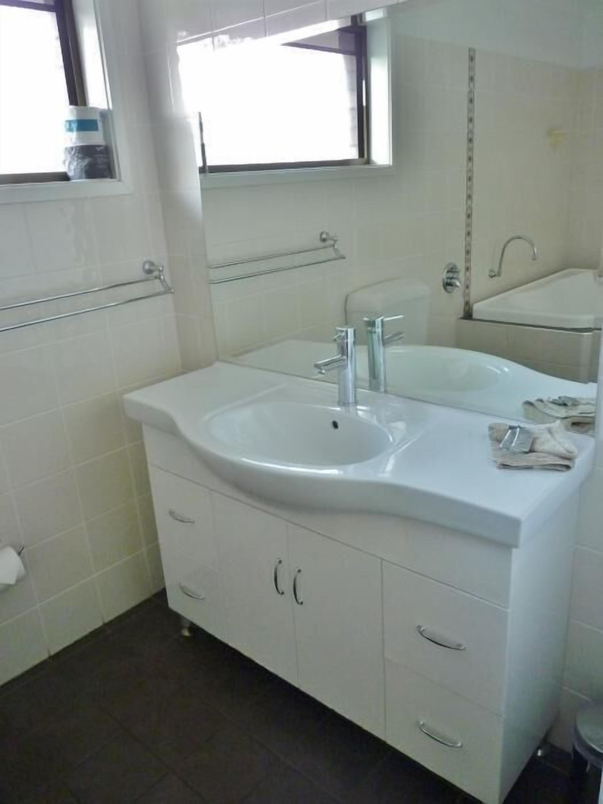Une salle de bain moderne avec un meuble-lavabo blanc, deux vasques, un miroir et un porte-serviettes.