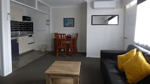 Un espacio habitable compacto con kitchenette, comedor y sofá de cuero negro con un cojín amarillo.