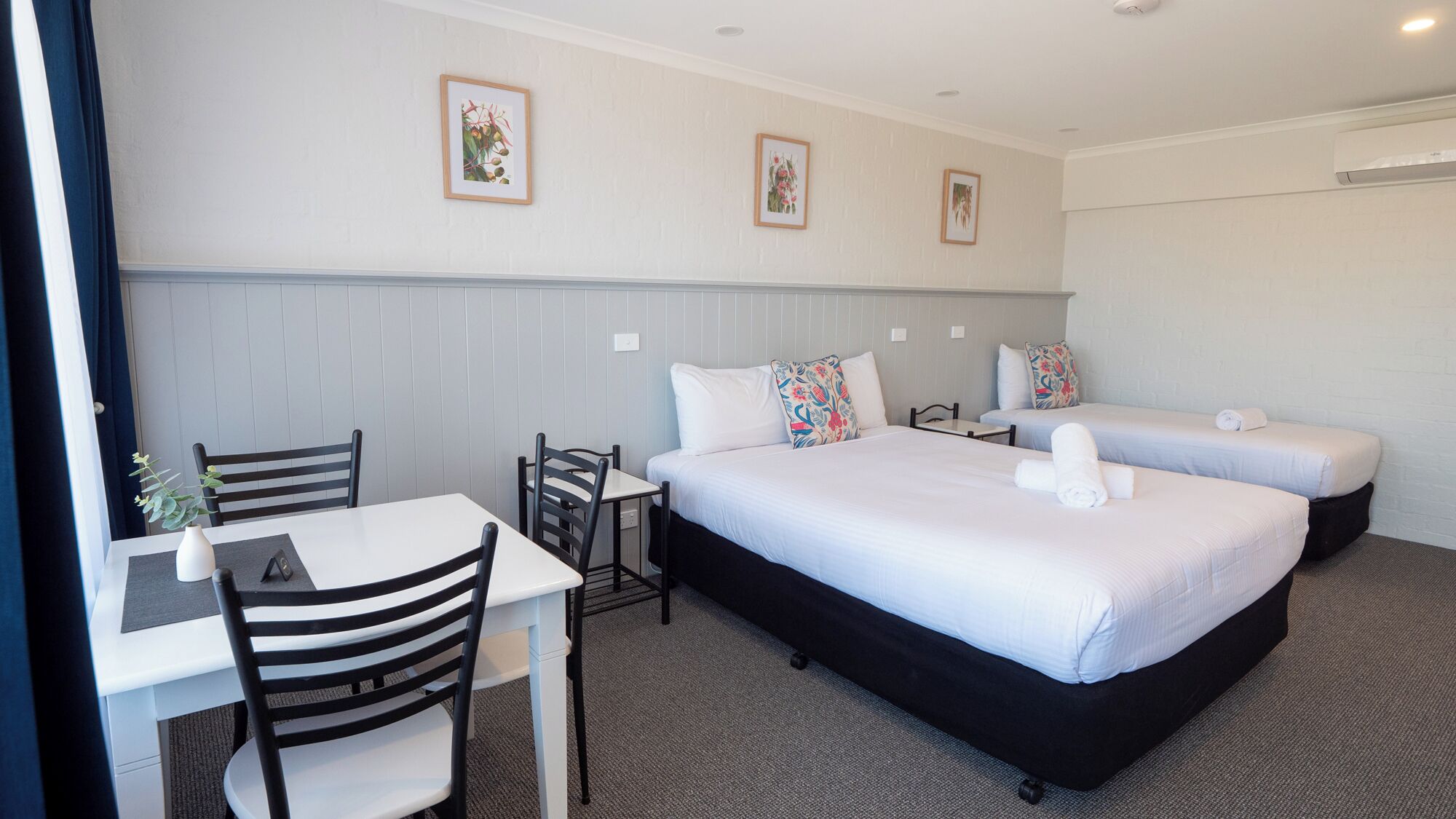 A hotel room with a bed, two bedside tables, a desk with a chair, and a small table with a plant.