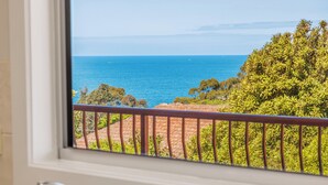 A view from a window overlooking a coastal landscape with a clear sky, a body of water, and greenery. - Heritage House Motel & Units (Eden)