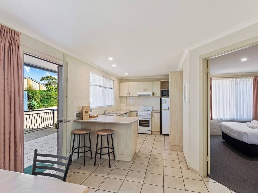 A compact hotel room with a kitchenette, a dining area with stools, and a bed.