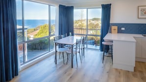 A modern kitchen with a large window overlooking a scenic view, a dining area with a table and chairs, and a small bar area. - Heritage House Motel & Units (Eden)