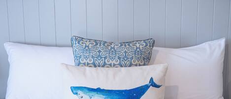 Ein Bett mit weißer Bettwäsche und zwei dekorativen Kissen, eines mit einem blauen Walmotiv und das andere mit blau-weißem Muster.
