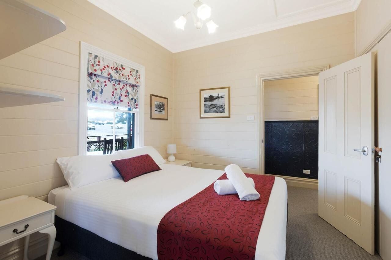 A hotel room with a bed, a nightstand, a window with a view, and a door.