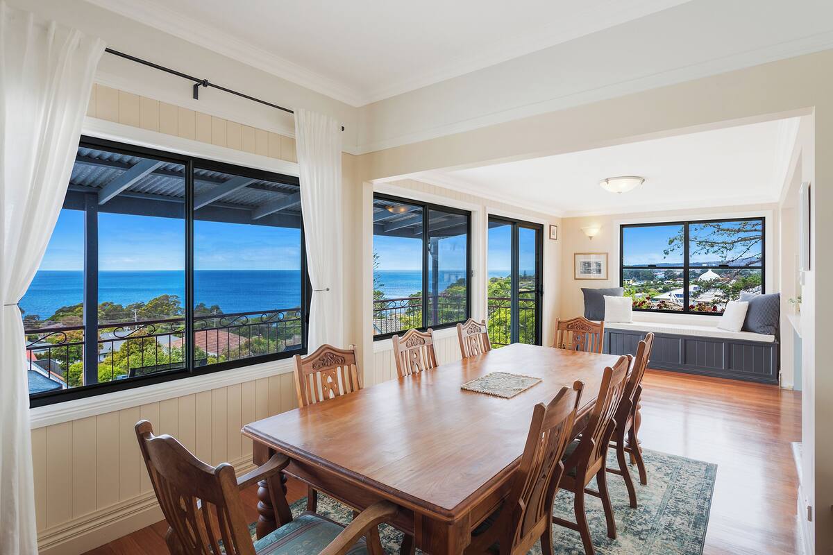 A dining area with a large table and chairs, large windows with ocean views, and a seating area with a view of the ocean.