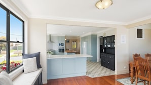 A modern kitchen with a large island, wooden flooring, and a view of the outdoors through a window. - Heritage House Motel & Units (Eden)