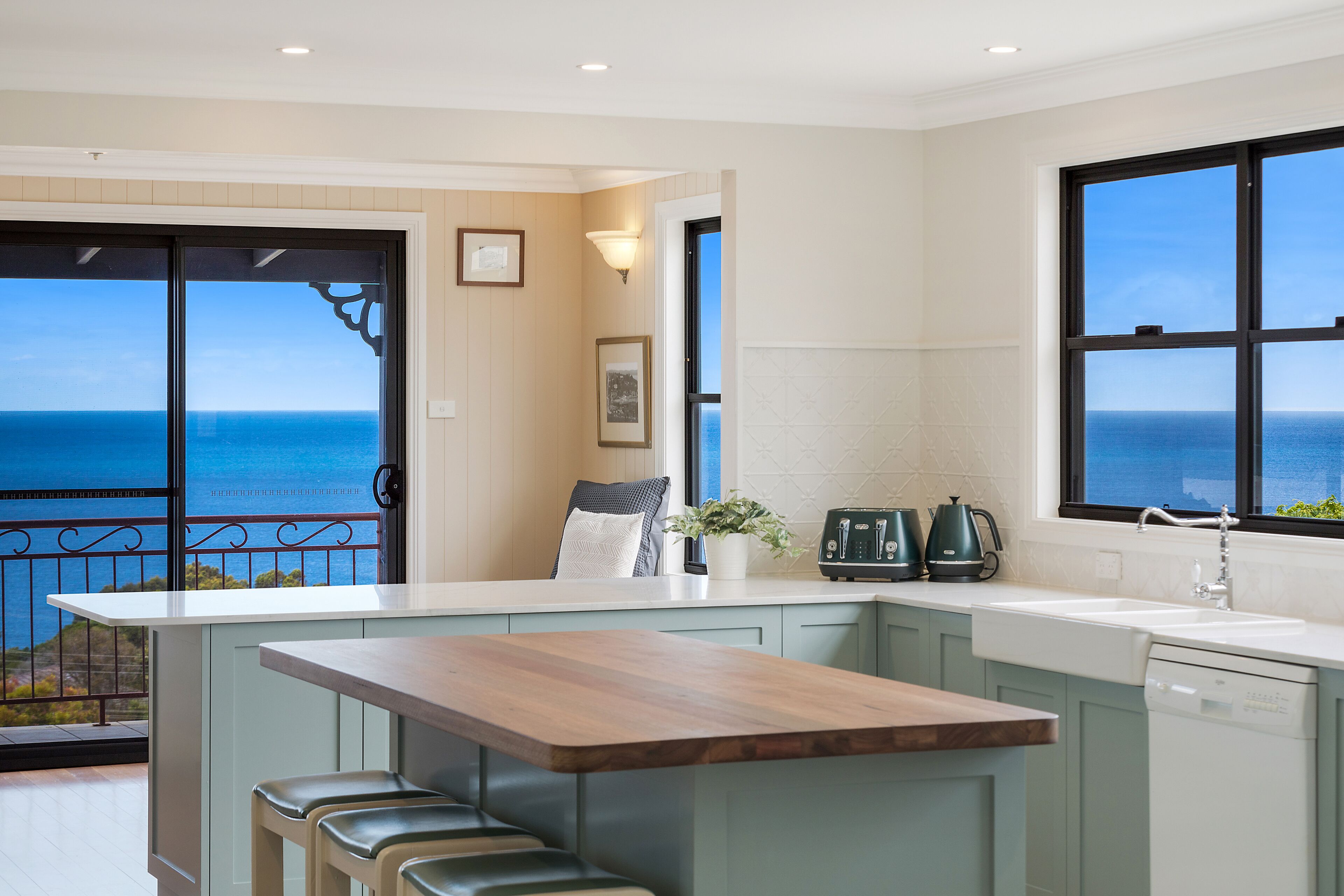 A kitchen with a view of the ocean, a wooden island with bar stools, and a window with a view.