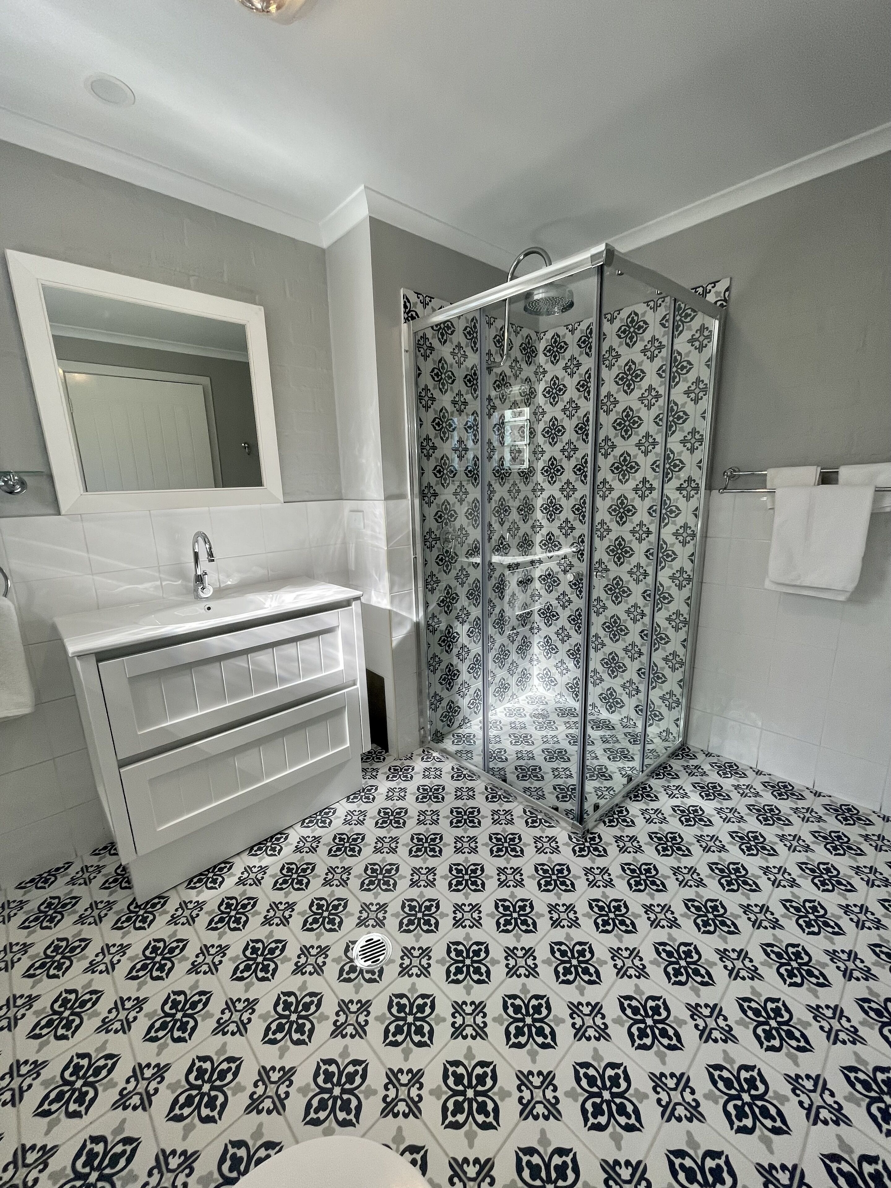 A bathroom with a white vanity, a glass shower enclosure, and patterned floor tiles.