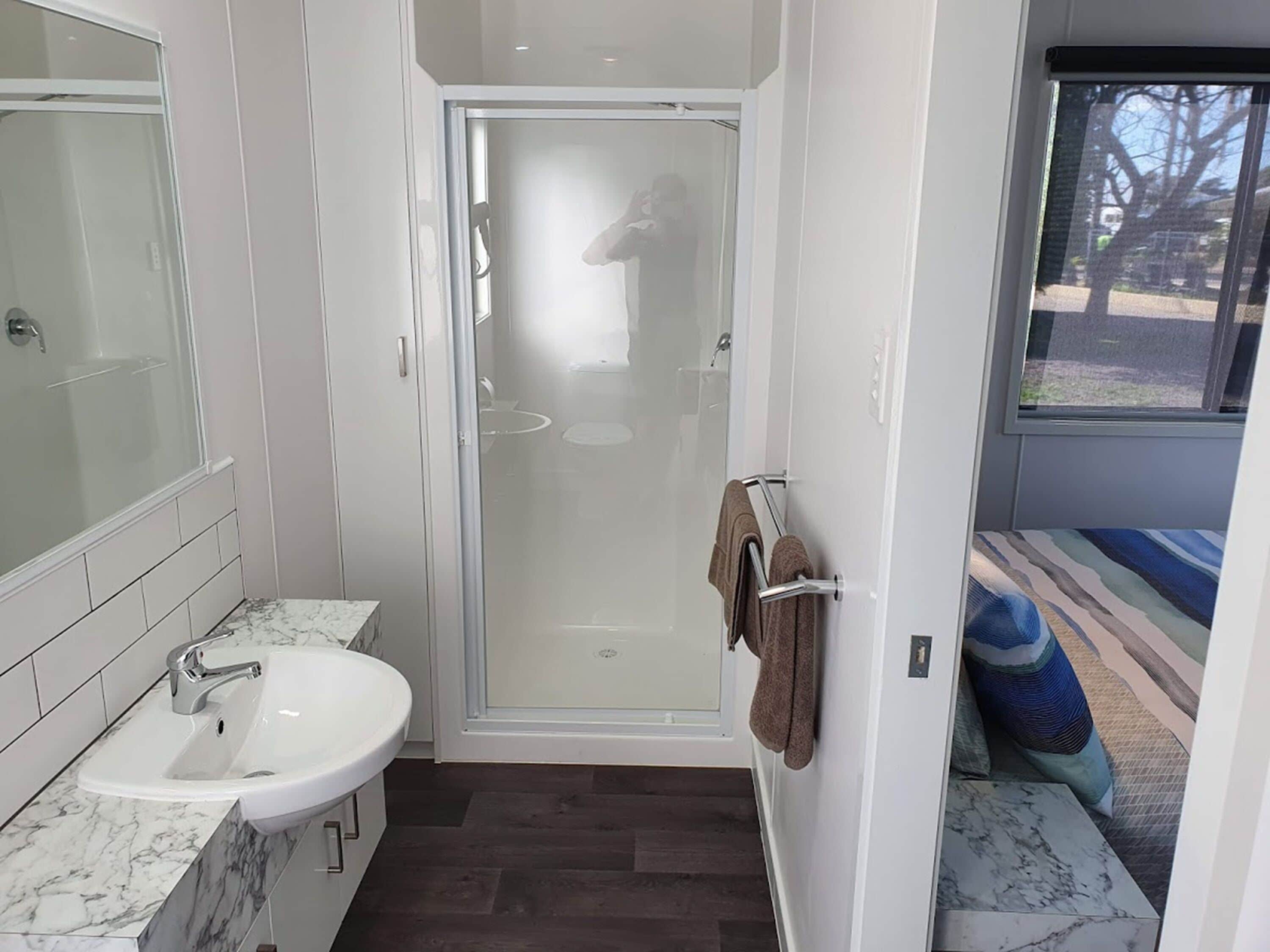 A modern bathroom with a glass-enclosed shower, a white sink with a marble countertop, and a towel rack with a brown towel.