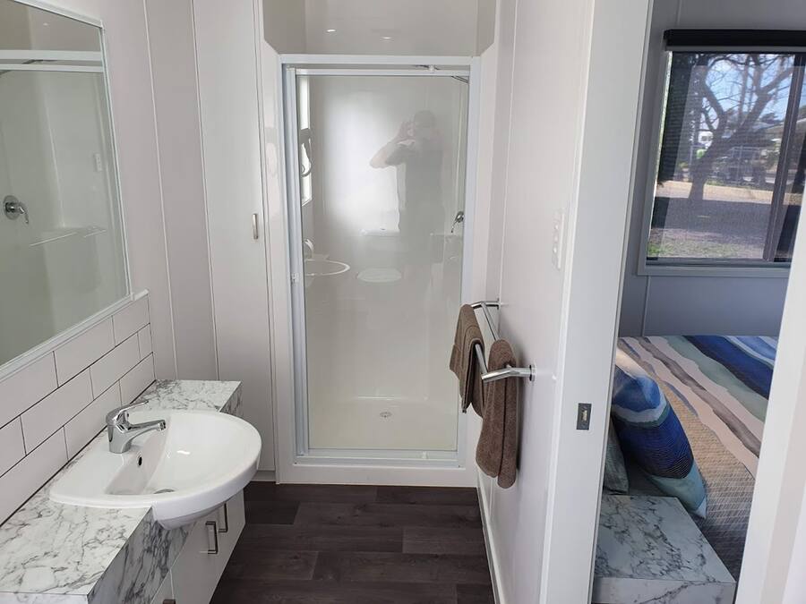A modern bathroom with a glass-enclosed shower, a white sink with a marble countertop, and a towel rack with a brown towel.