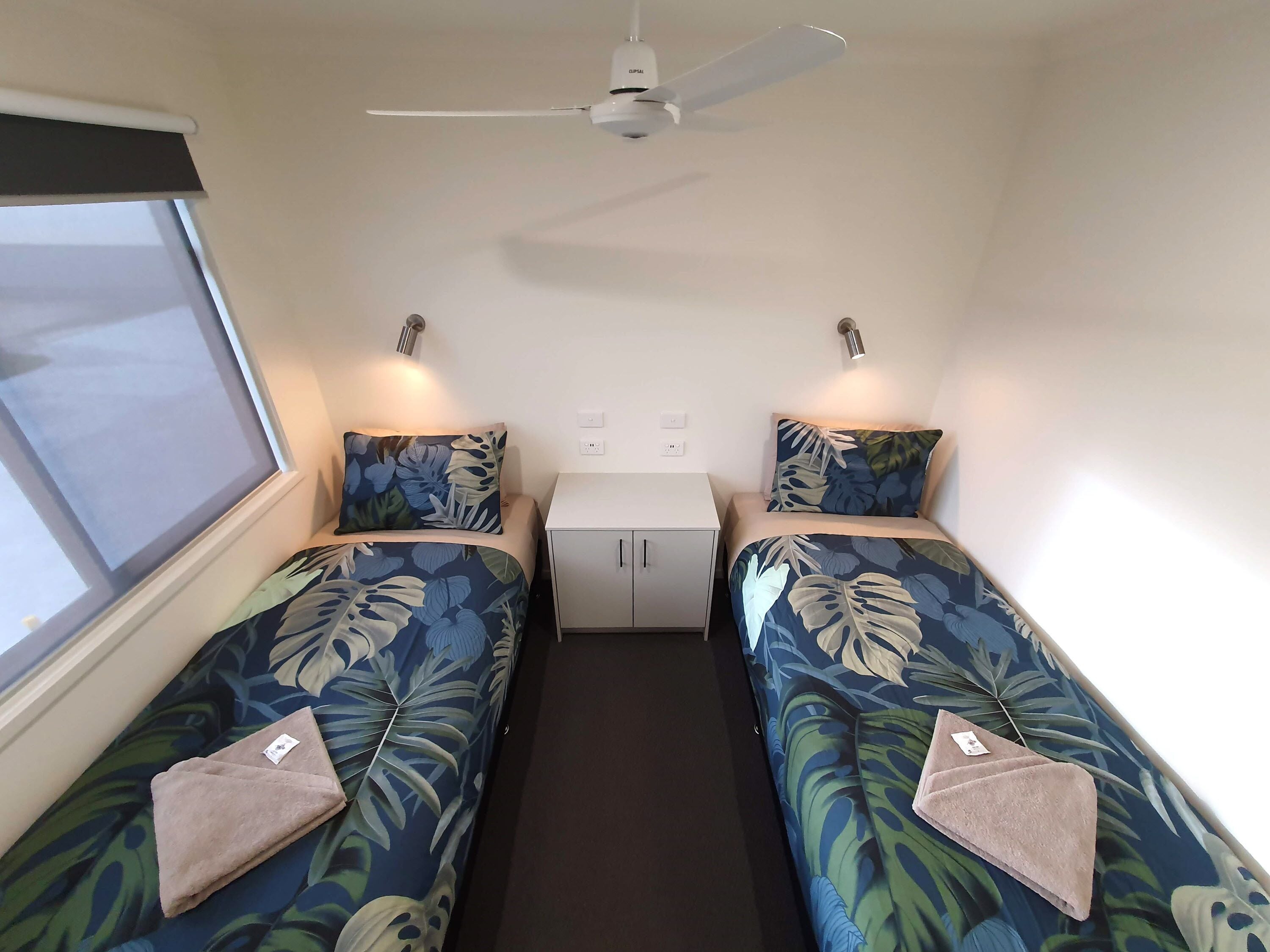 A compact room with two single beds, a small table, a ceiling fan, and a window.