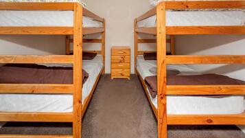 Een kamer met twee stapelbedden, elk voorzien van een kussen en dekbed, en een klein houten dressoir daartussen.