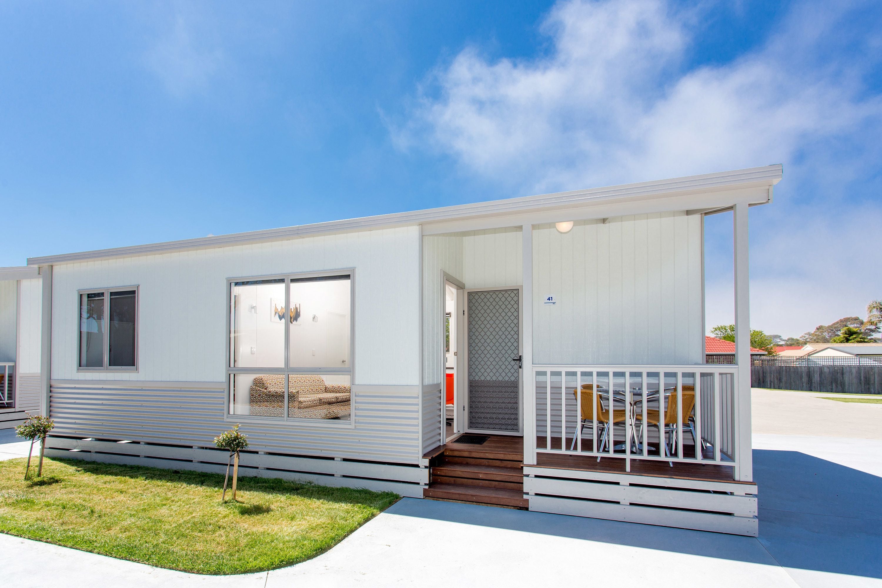 A single-story mobile home with a porch, a small front yard, and a clear blue sky.