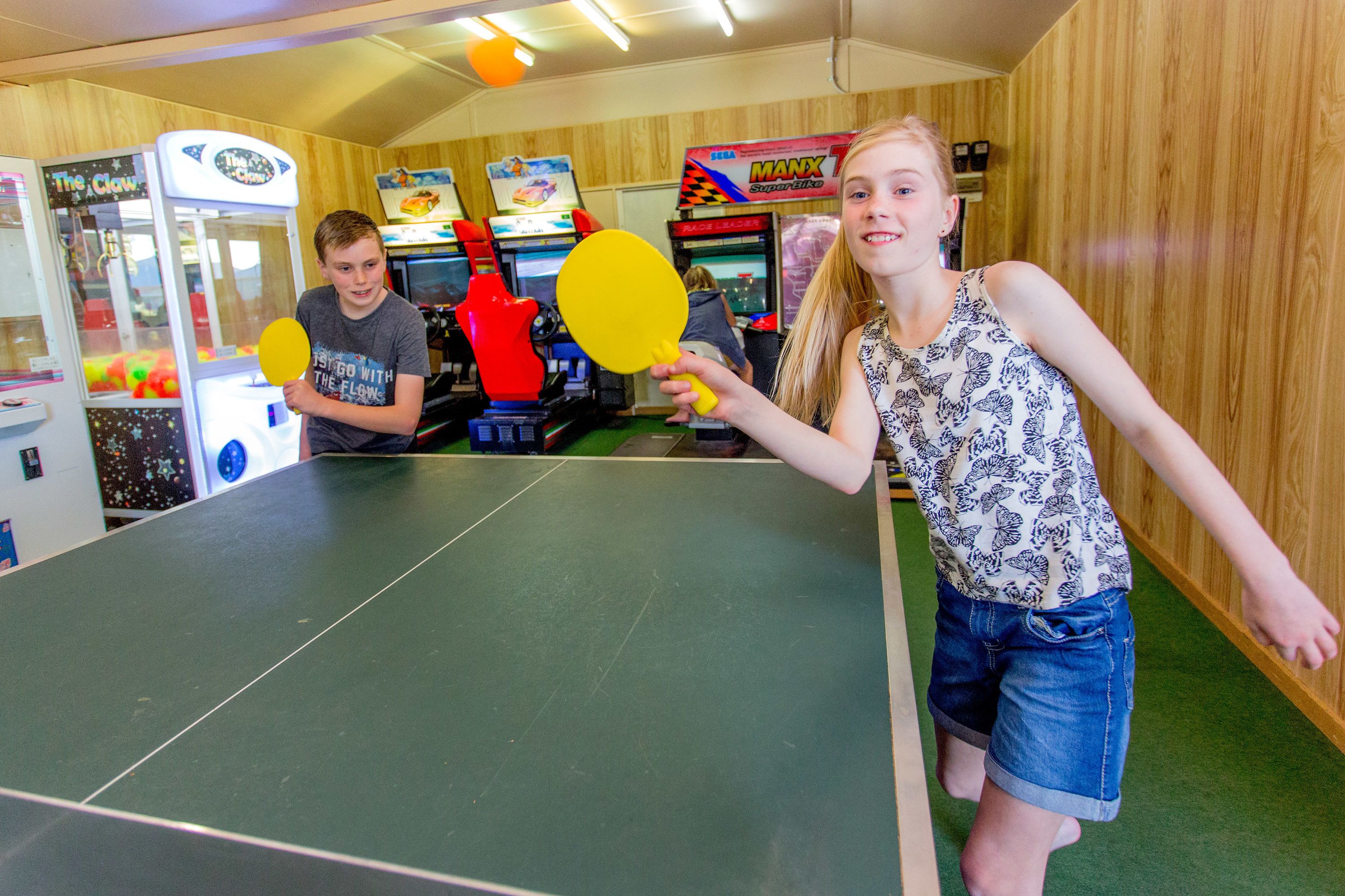 A ping pong table in a room with wooden walls, arcade games, and claw machines.