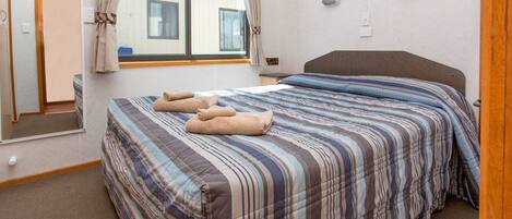 A hotel room with a large bed, a window with curtains, a bedside table, and a mirror.