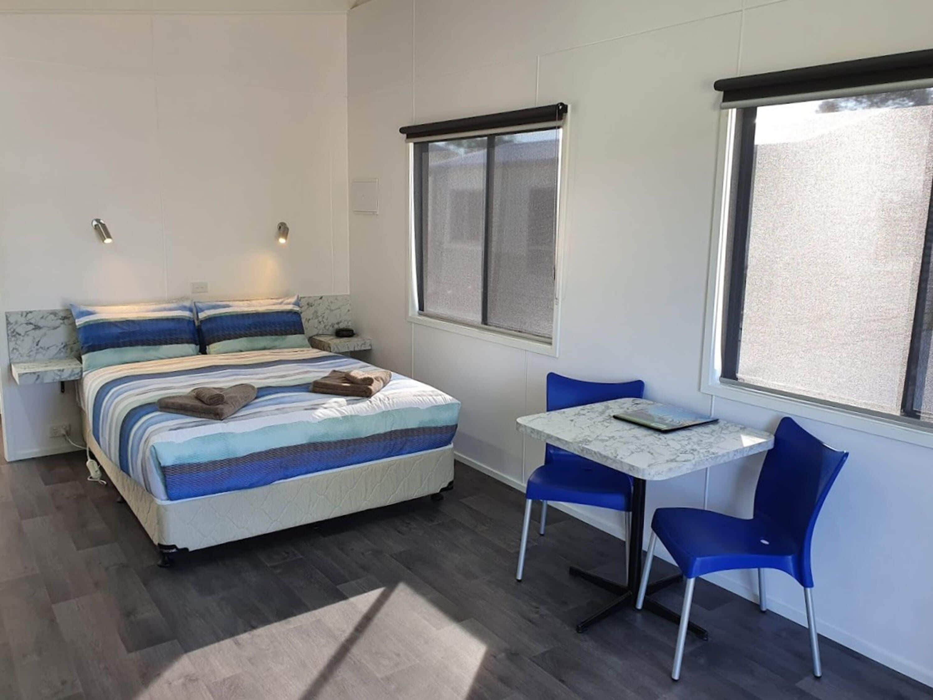 A bedroom with a bed, two bedside tables, a window, and a small table with two chairs.