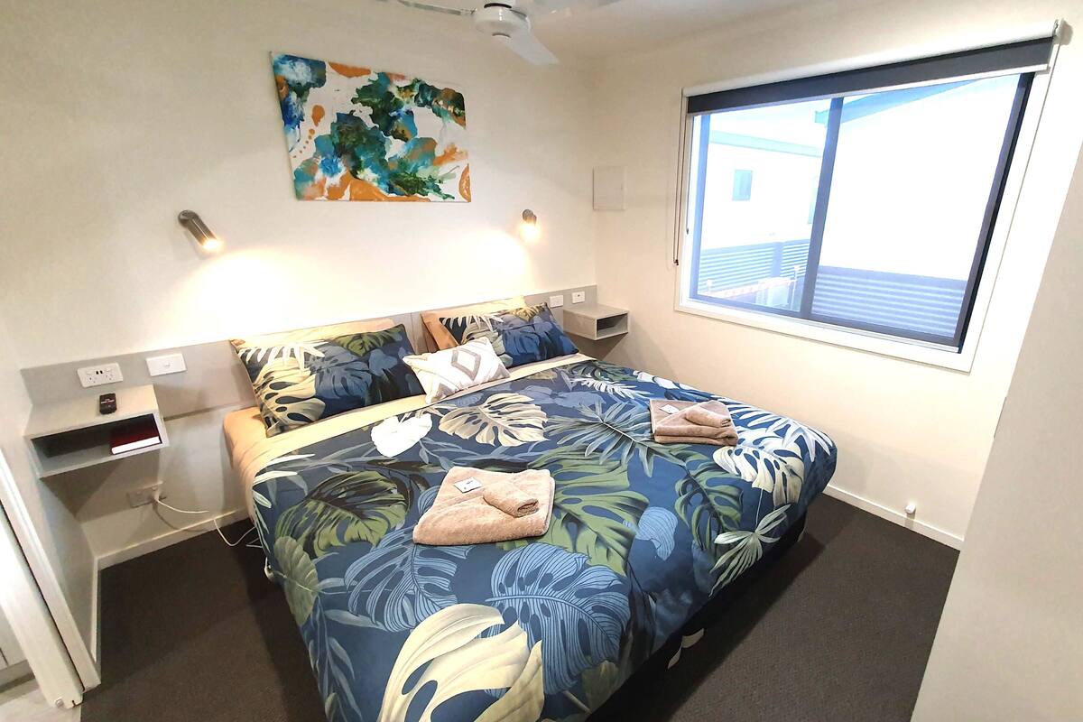 Una camera da letto con una coperta a fiori, un quadro appeso al muro e una finestra con persiane.