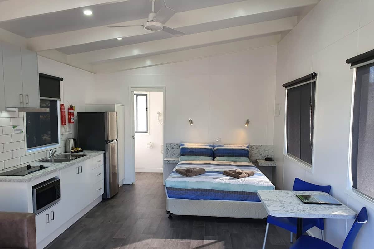Camera d'albergo compatta con angolo cottura, un letto con copripiumino a righe blu e bianche e un piccolo tavolo da pranzo con sedie blu.