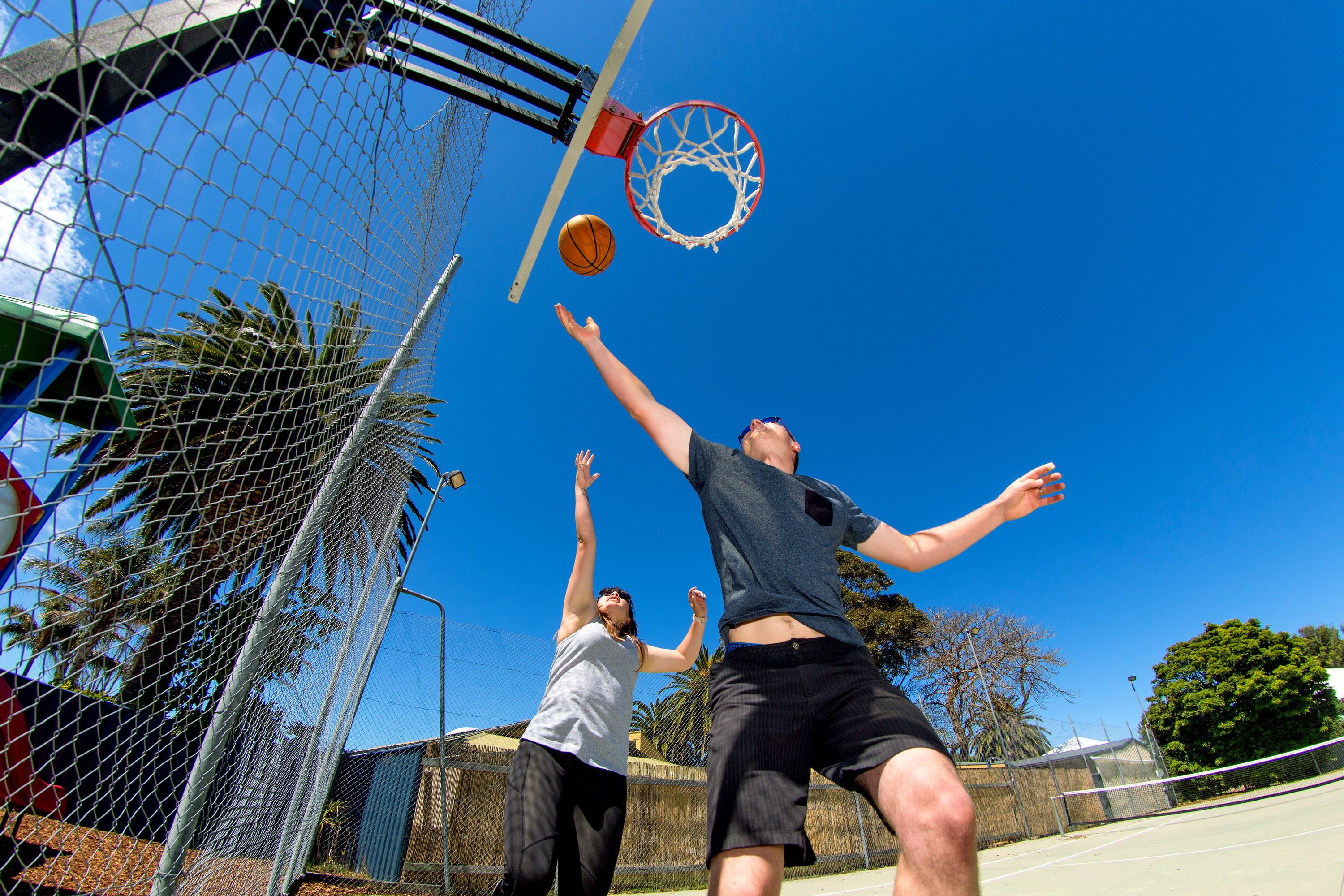 Una cancha de baloncesto con aro y red, y dos personas jugando.