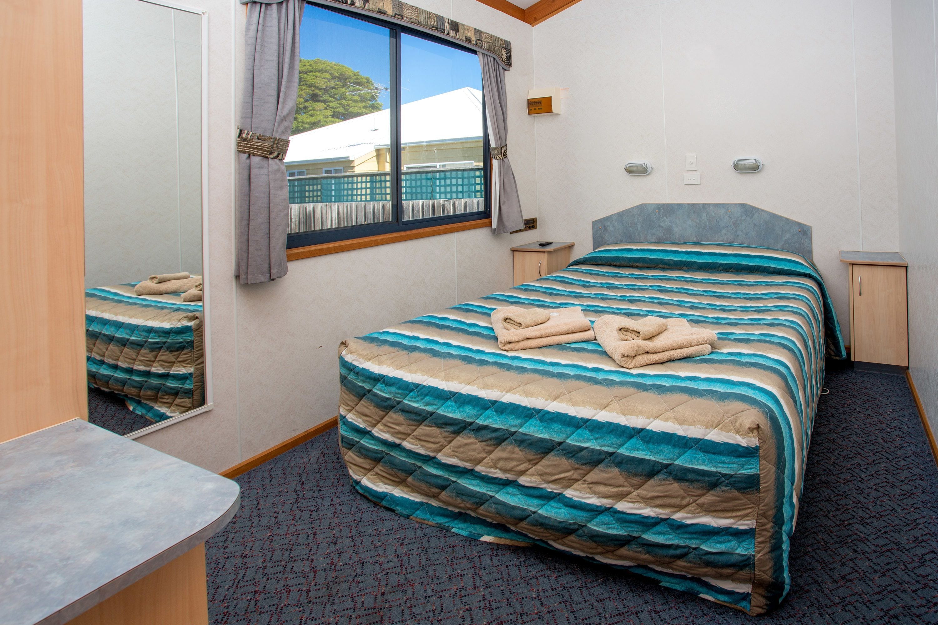 A hotel room with a large bed, a bedside table, a nightstand, a mirror, and a window with curtains.