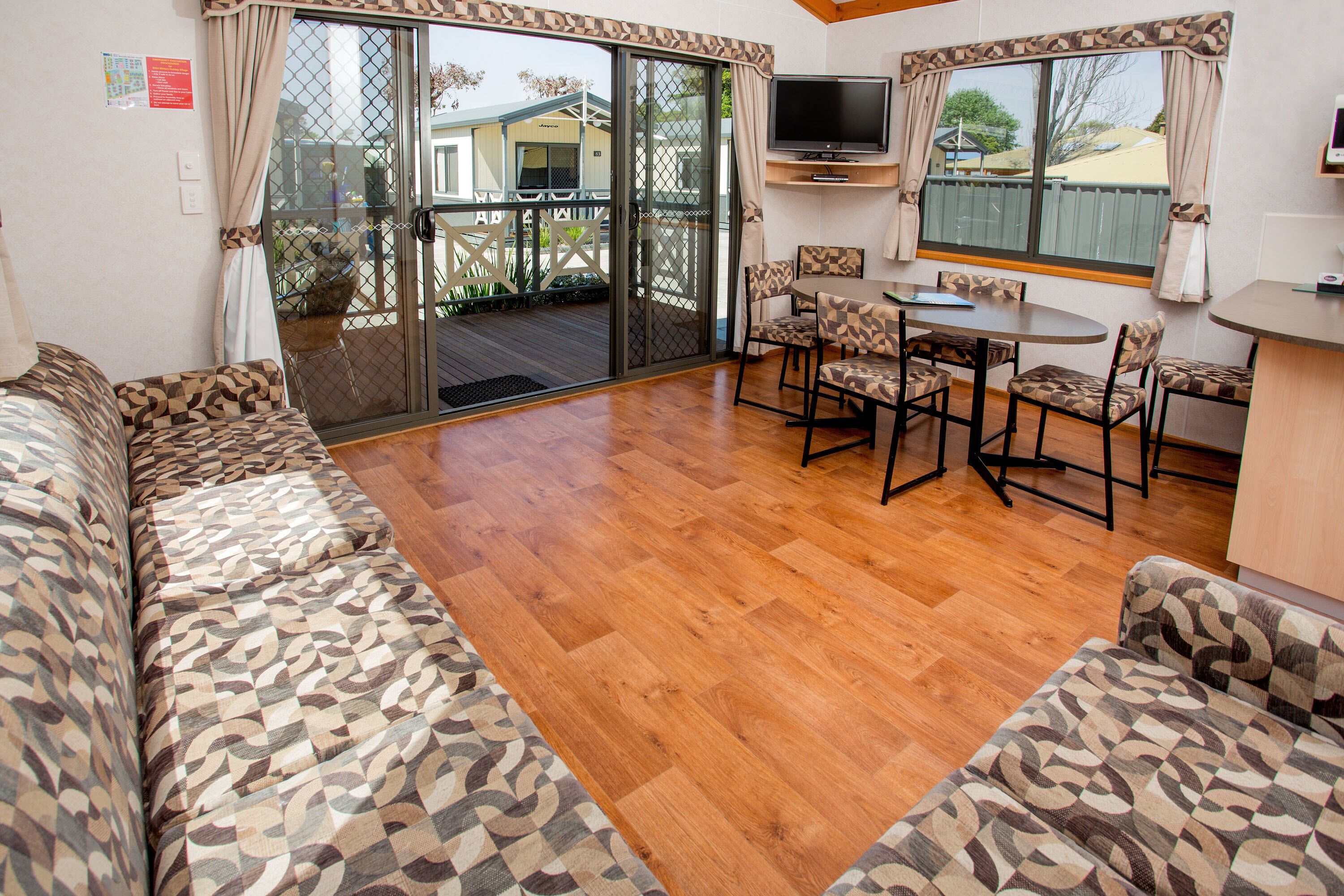 Une pièce avec un plancher en bois, un canapé à motifs, une table à manger avec des chaises et un téléviseur fixé au mur.