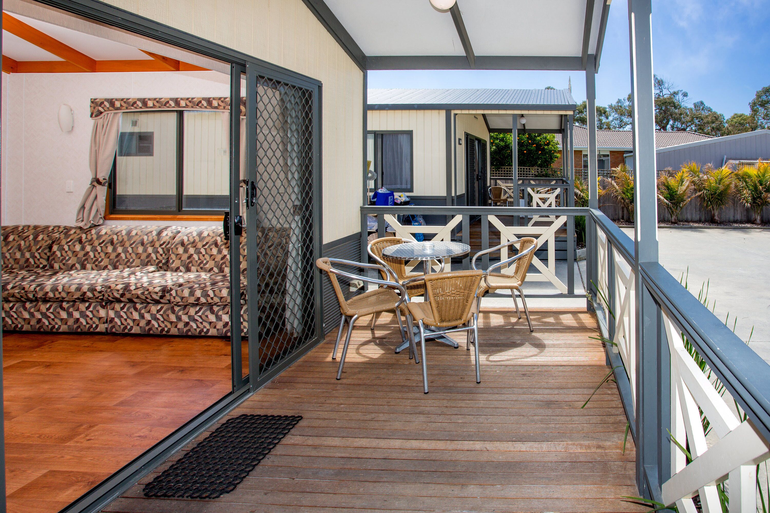 A covered outdoor area with a wooden deck, wicker chairs, a small table, and a sofa.